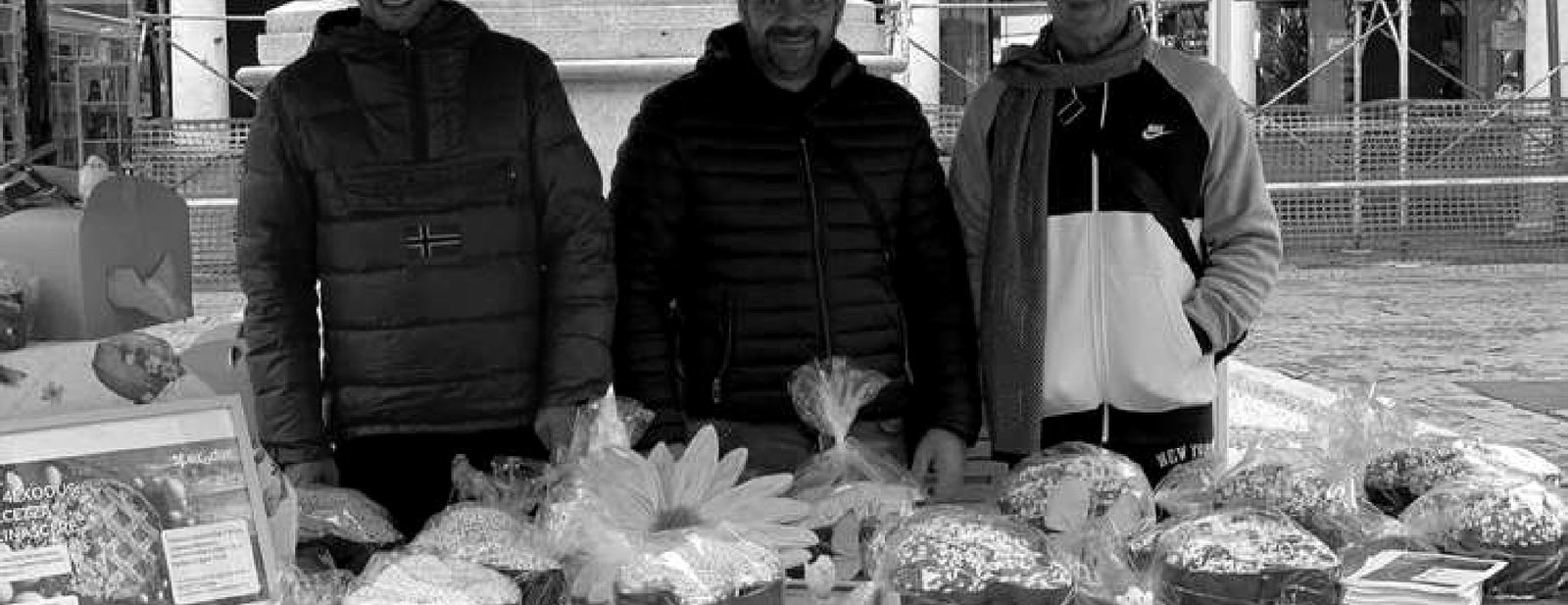 Tre persone dietro il banco di un mercatino con dolci e prodotti artigianali